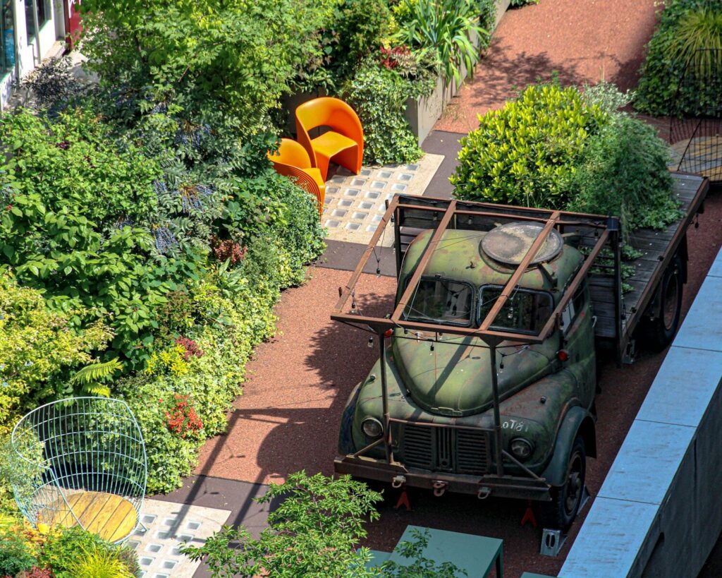 Old green truck surrounded by lush urban garden plants